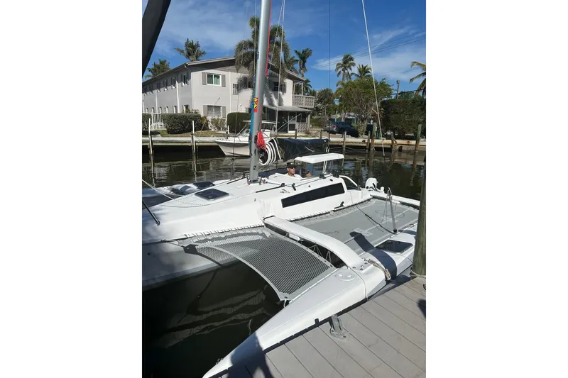Slide: The Image of 2025 Corsair 760 trimaran docked near waterfront homes, under clear blue skies. - 3
