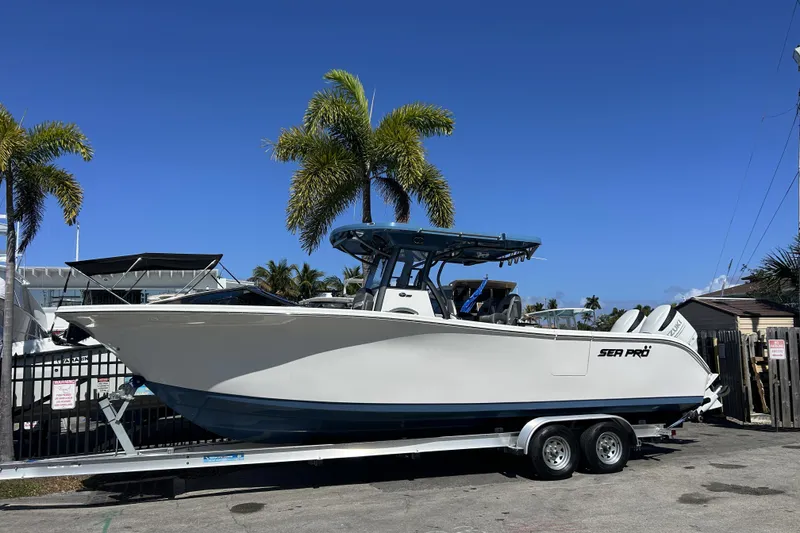 The Image of 2026 Sea Pro 292 DLX boat on trailer, parked near palm trees under clear blue sky. - 0