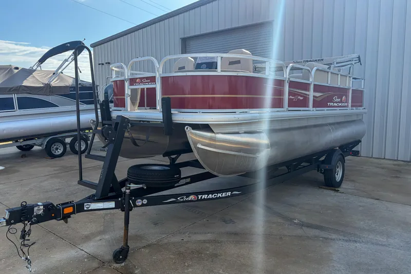 Slide: The Image of 2024 Sun Tracker Bass Buggy 18 DLX pontoon boat on trailer, parked outdoors. - 4
