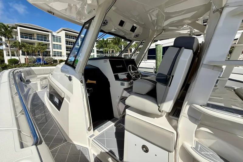 Slide: The Image of 2022 Pursuit S 428 Sport boat interior with helm and seating, docked near modern buildings. - 37