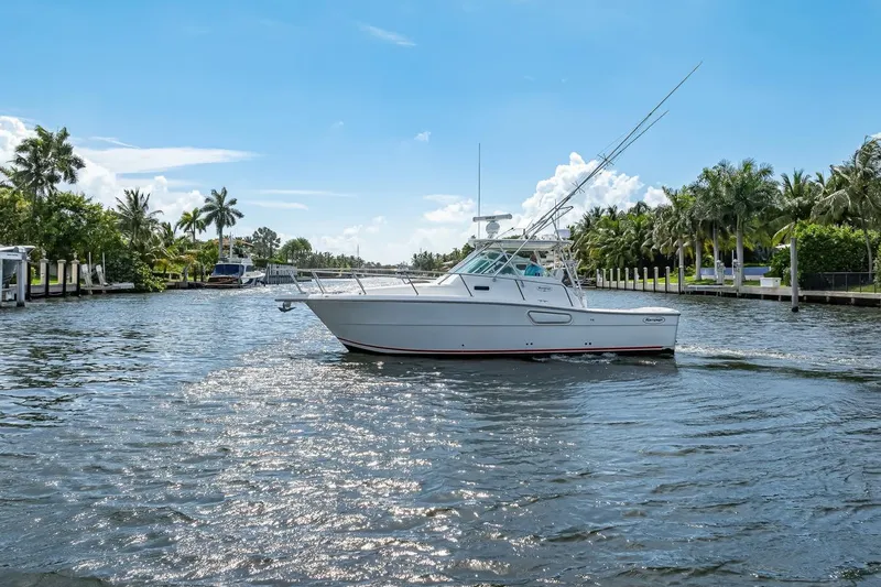 Slide: The Image of 2000 Rampage 30 Express boat cruising on a sunny, palm-lined waterway. - 4