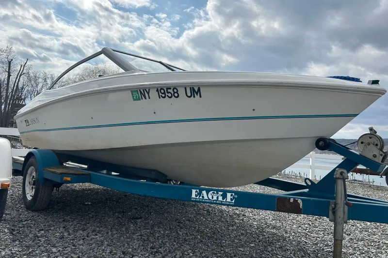 Slide: The Image of 1993 Larson All American 160 boat on trailer, parked on gravel near a lake. - 4