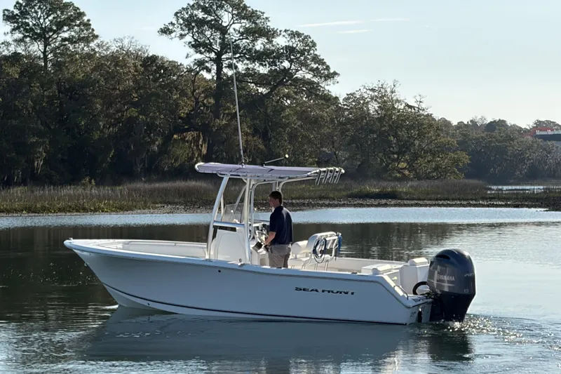 Slide: The Image of 2014 Sea Hunt Triton 225 boat cruising on a calm river with scenic forest backdrop. - 33