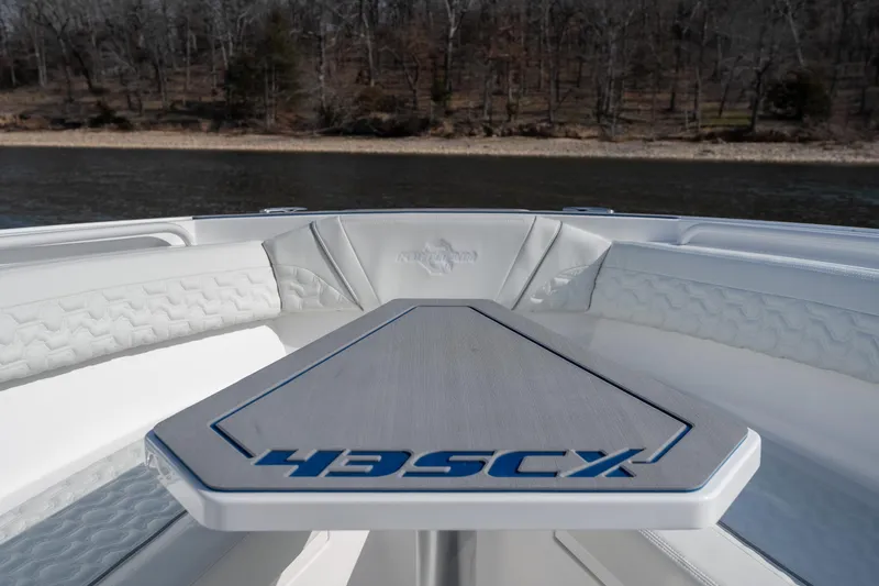Slide: The Image of 2026 Fountain 43 SCX boat interior with sleek seating and table, near a wooded shoreline. - 13