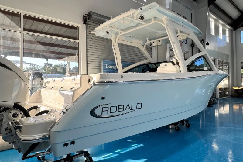Slide: The Image of 2026 Robalo R277 Dual Console boat displayed indoors on a blue floor. - 8