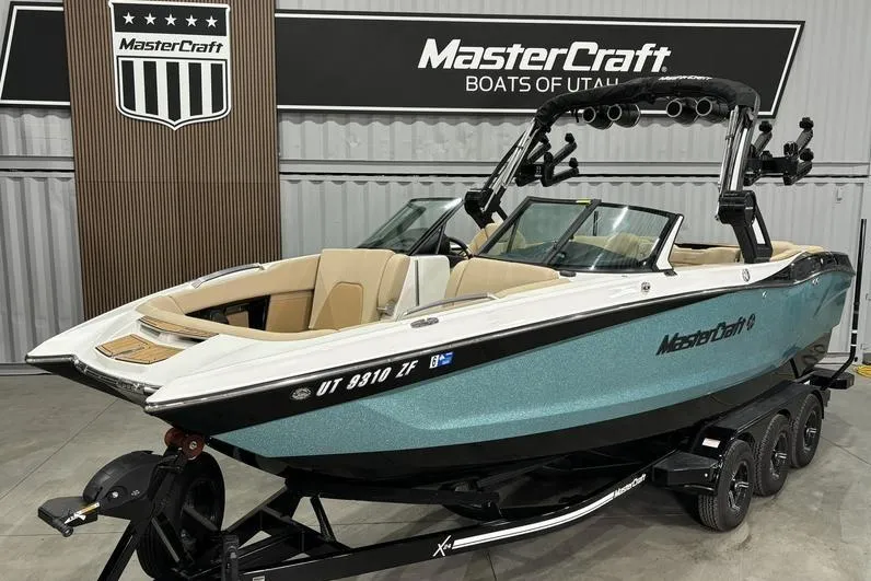 The Image of 2024 MasterCraft X24 boat in showroom, teal and black design, on trailer. - 1