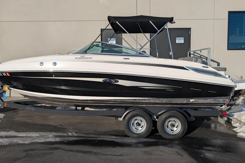 The Image of 2011 Sea Ray 240 Sundeck boat on trailer, black and white exterior, parked outdoors. - 0
