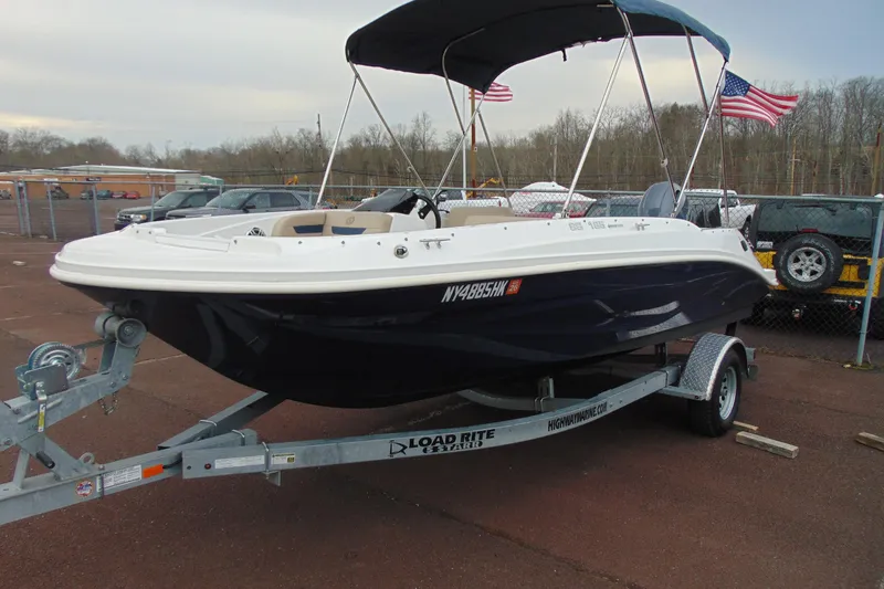 Slide: The Image of 2023 Hurricane SunDeck Sport 185 OB boat on trailer, parked outdoors with American flags. - 4