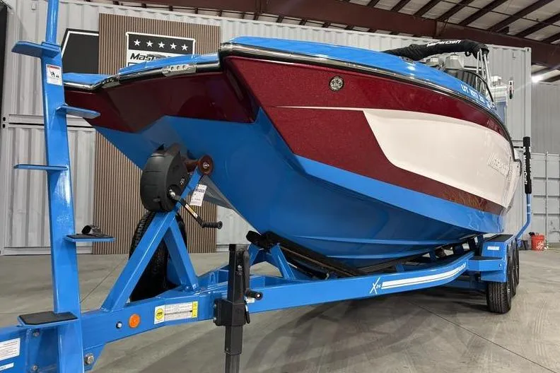 Slide: The Image of 2024 MasterCraft X24 boat on blue trailer in indoor showroom. - 2