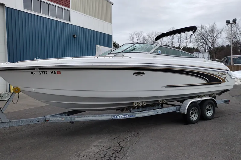 Slide: The Image of 2004 Formula 260 Bowrider boat on trailer, parked outdoors near a blue building. - 2