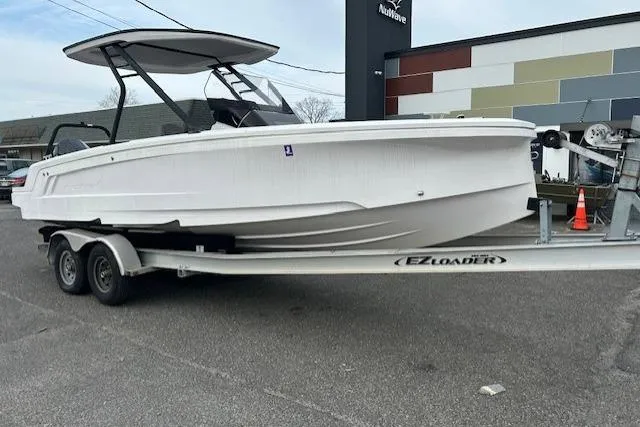 The Image of 2022 Axopar 22 T-Top boat on trailer, parked outdoors near a modern building. - 0