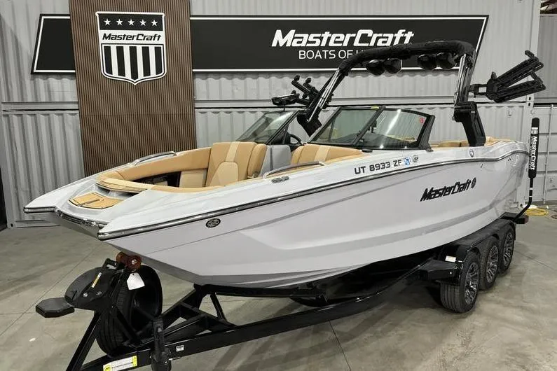 The Image of 2024 MasterCraft X24 boat on trailer in showroom, featuring sleek design and luxury seating. - 1