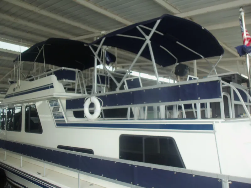 Slide: The Image of 2003 Gibson Classic houseboat with blue canopy and white exterior, docked under a shelter. - 4