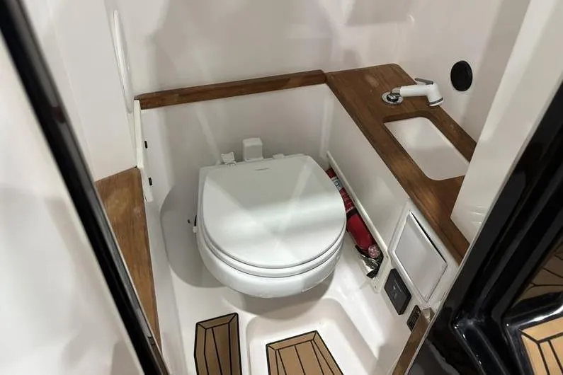 Slide: The Image of 2024 MasterCraft X26 boat bathroom with toilet, sink, and wooden accents. - 15