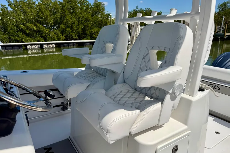Slide: The Image of 2021 Sportsman Open 302 Center Console boat seats with armrests, docked near lush greenery. - 8