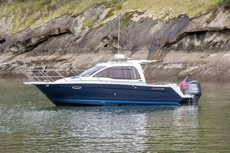 Slide: The Image of Manufacturer Provided Image: 2022 Cutwater C-24 Coupe boat on calm water near rocky shoreline. - 3