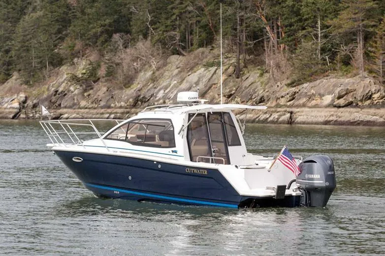 Slide: The Image of Manufacturer Provided Image: 2022 Cutwater C-24 Coupe boat cruising on a scenic lake with forested shoreline. - 4