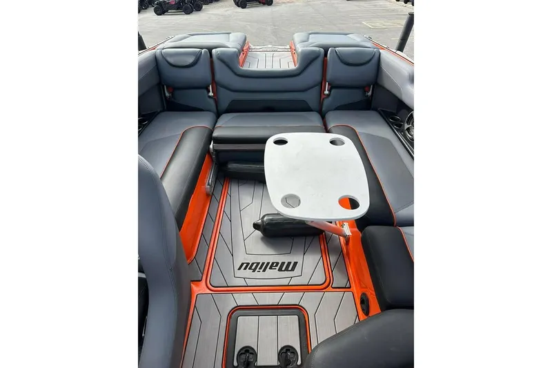 Slide: The Image of 2017 Malibu M235 boat interior with gray and orange seating, table, and logo. - 12