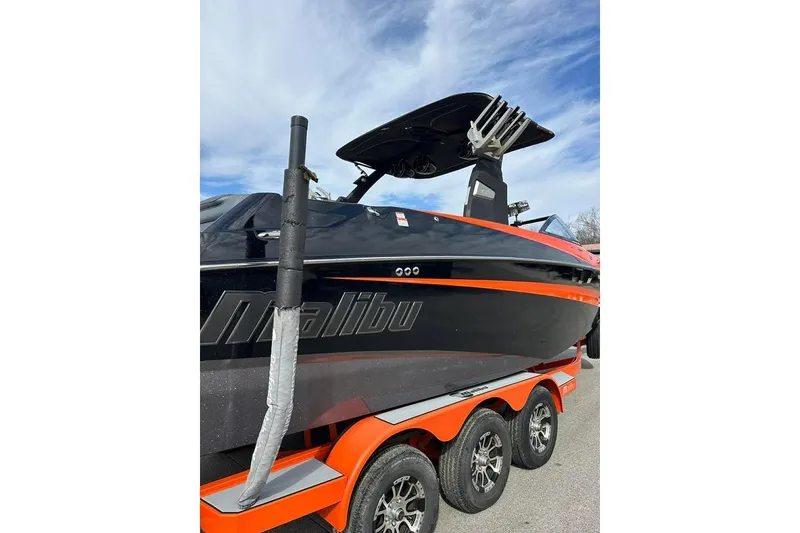Slide: The Image of 2017 Malibu M235 boat on trailer, black and orange design, under blue sky. - 5