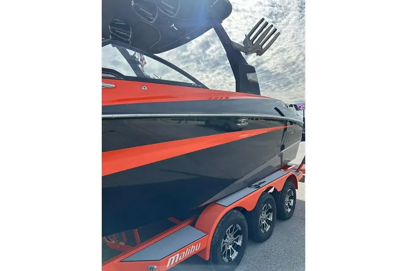 Slide: The Image of 2017 Malibu M235 boat with vibrant orange and black design on a triple-axle trailer. - 6