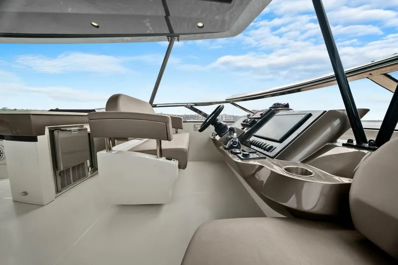 Slide: The Image of 2014 Marquis 630 Sport Yacht helm with modern controls and seating, under a clear blue sky. - 29