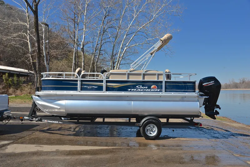 Slide: The Image of 2024 Sun Tracker Bass Buggy 18 DLX pontoon boat on trailer by a lake. - 11
