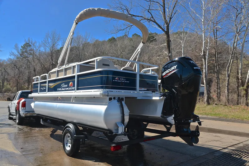 Slide: The Image of 2024 Sun Tracker Bass Buggy 18 DLX pontoon boat on trailer, parked near trees. - 12