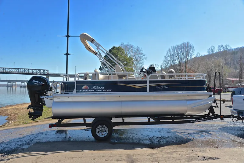 Slide: The Image of 2024 Sun Tracker Bass Buggy 18 DLX pontoon boat on trailer by a lake. - 15