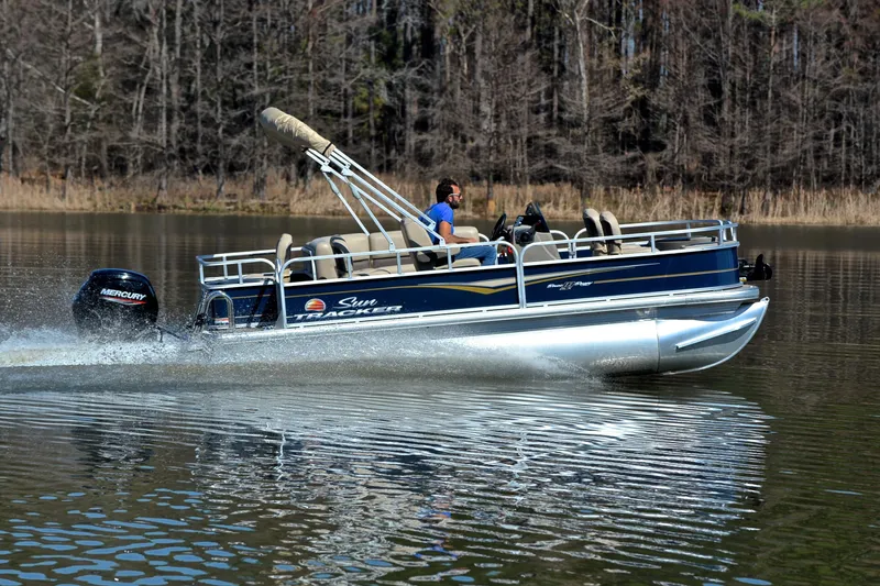 Slide: The Image of 2024 Sun Tracker Bass Buggy 18 DLX pontoon boat cruising on a calm lake. - 3