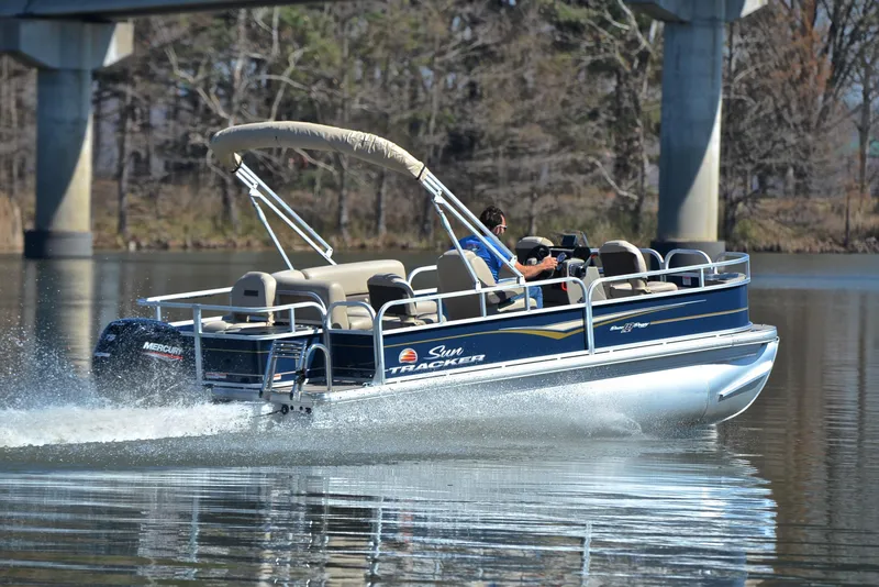 Slide: The Image of 2024 Sun Tracker Bass Buggy 18 DLX pontoon boat cruising on a calm lake. - 5