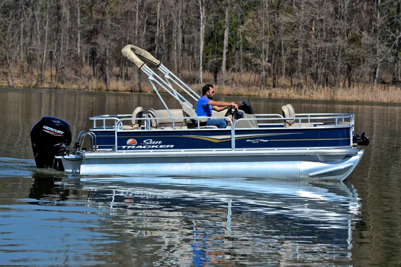 Slide: The Image of 2024 Sun Tracker Bass Buggy 18 DLX pontoon boat cruising on a calm lake. - 6