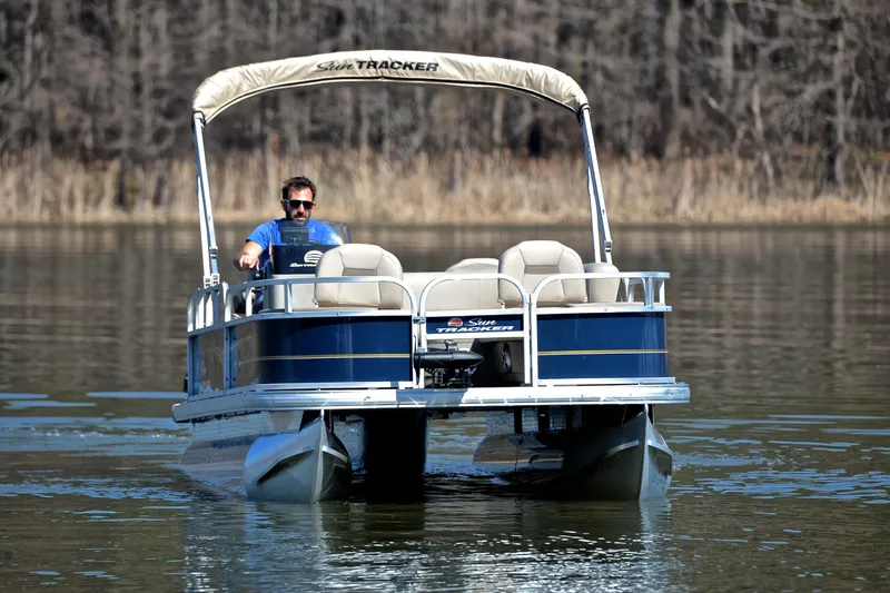 Slide: The Image of 2024 Sun Tracker Bass Buggy 18 DLX pontoon boat cruising on a calm lake. - 8