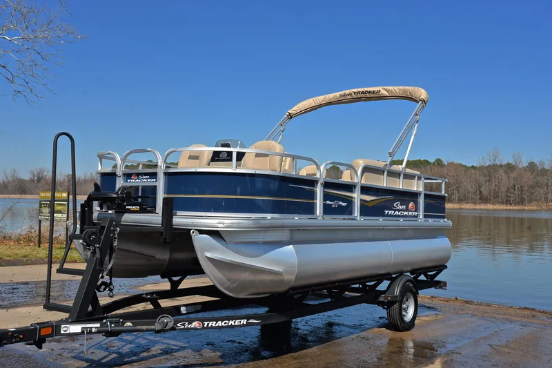 Slide: The Image of 2024 Sun Tracker Bass Buggy 18 DLX pontoon boat on trailer by a lake. - 9