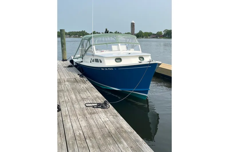 Slide: The Image of 1970 Brownell Cuttyhunk boat docked on calm water, featuring a blue and white design. - 2