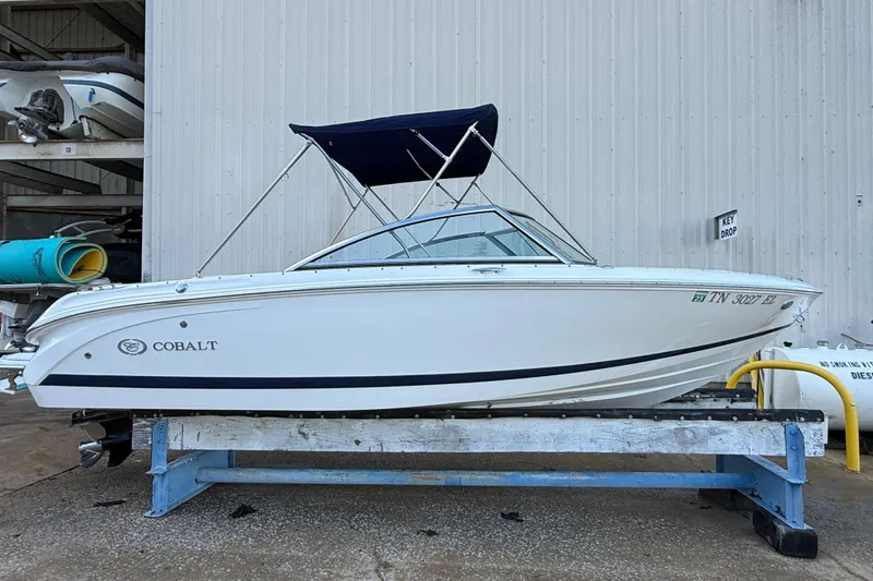 The Image of 2015 Cobalt 200 boat with blue canopy on a trailer, parked near a warehouse. - 0