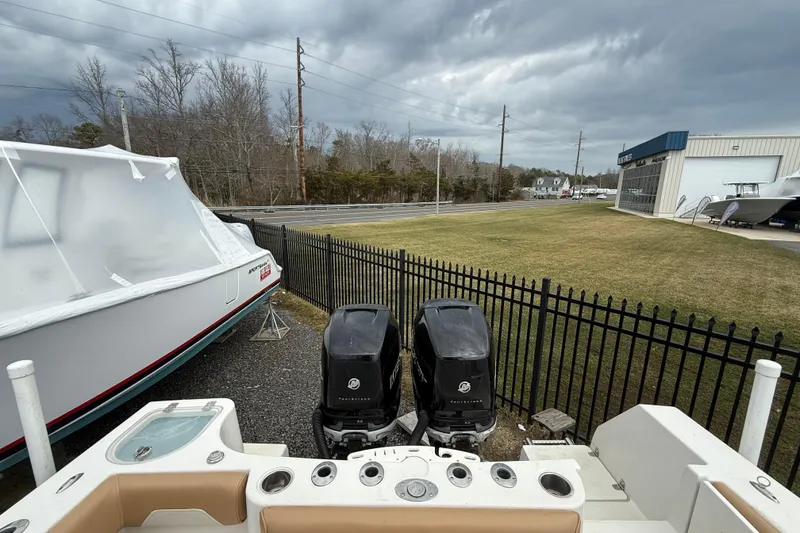 Slide: The Image of 2015 Sailfish 2860 CC boat with dual outboard motors, parked near a fenced area. - 6