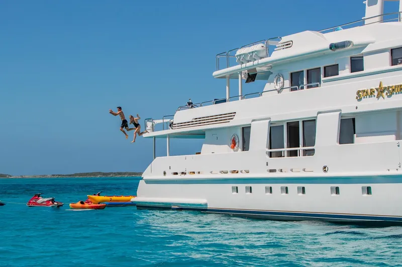 Slide: The Image of Two people jumping off a 1988 Van Mill Custom yacht into the ocean, surrounded by kayaks. - 110