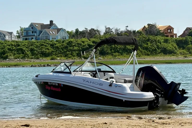 Slide: The Image of 2016 Tahoe 450 TS boat docked on a sandy shore with houses in the background. - 2