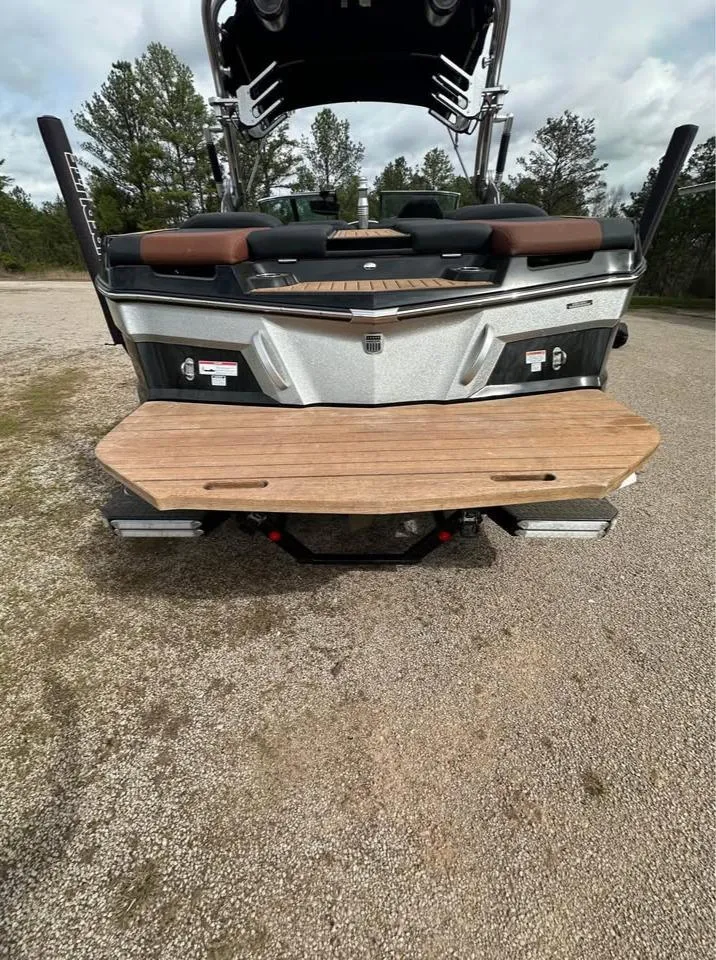 Slide: The Image of 2021 MasterCraft XT22 boat rear view with teak swim platform, parked on gravel. - 7