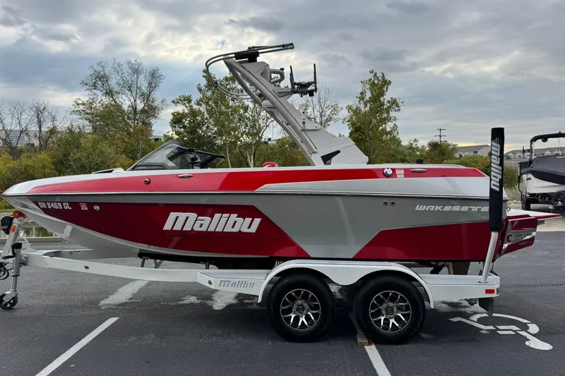 Slide: The Image of 2023 Malibu Wakesetter 20 VTX boat in red and gray on a trailer, parked outdoors. - 6