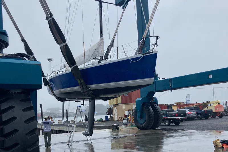 Slide: The Image of A 1995 Tripp 47 sailboat being lifted by a large crane at a marina. - 10