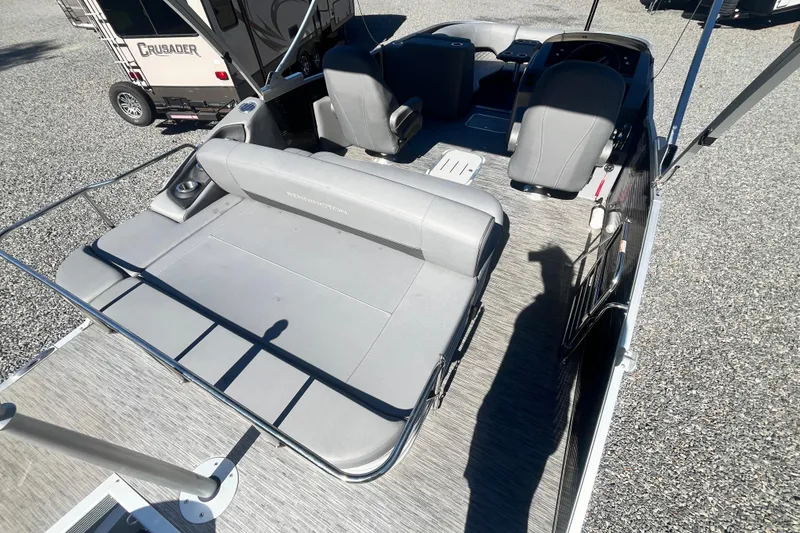 Slide: The Image of 2022 Bennington 23LT pontoon boat interior with gray seating and helm, parked on gravel. - 12