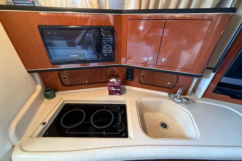 Slide: The Image of 2003 Sea Ray 300 Sundancer kitchen with stove, sink, microwave, and wooden cabinets. - 35