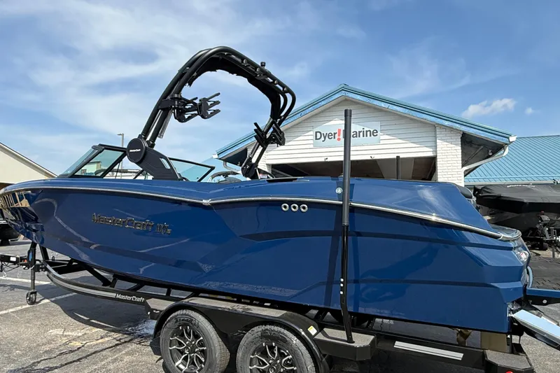 Slide: The Image of 2026 MasterCraft NXT24 boat in blue, parked at Dyer Marine dealership. - 2