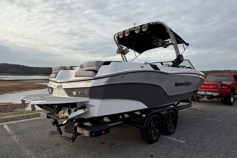 Slide: The Image of 2023 MasterCraft XT24 boat on trailer, parked near a lake with a cloudy sky. - 4