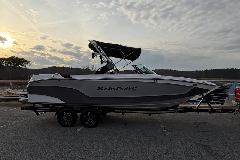 Slide: The Image of 2023 MasterCraft XT24 boat on trailer at sunset, parked near a lake. - 6