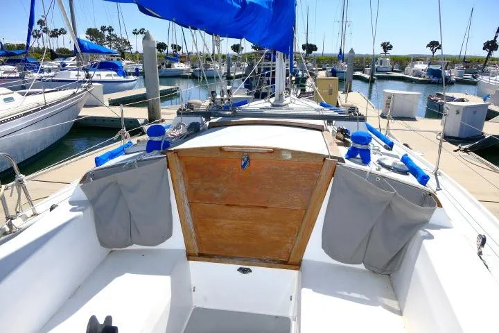 Slide: The Image of 1989 Catalina 34 sailboat docked in marina, featuring blue sails and wooden hatch. - 49