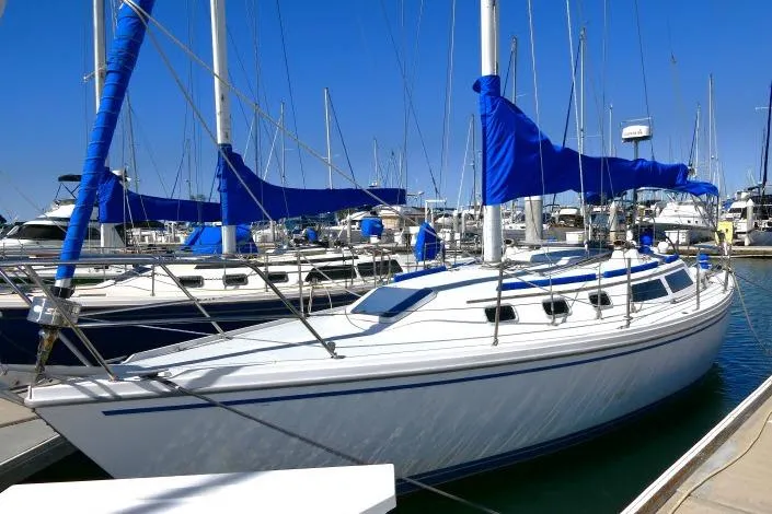 Slide: The Image of 1989 Catalina 34 sailboat docked in marina, featuring blue sails and clear sky. - 77