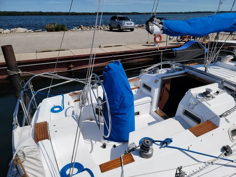 Slide: The Image of 1984 Hunter 34 sailboat docked, featuring blue covers and a scenic waterfront view. - 30