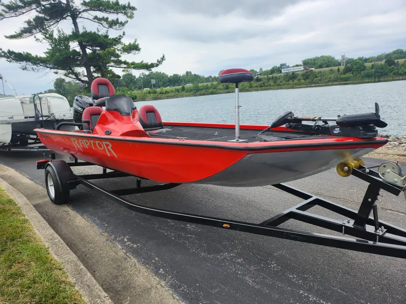 Slide: The Image of 2021 Caravelle Raptor 180 Bass boat in red, parked by a lakeside. - 9